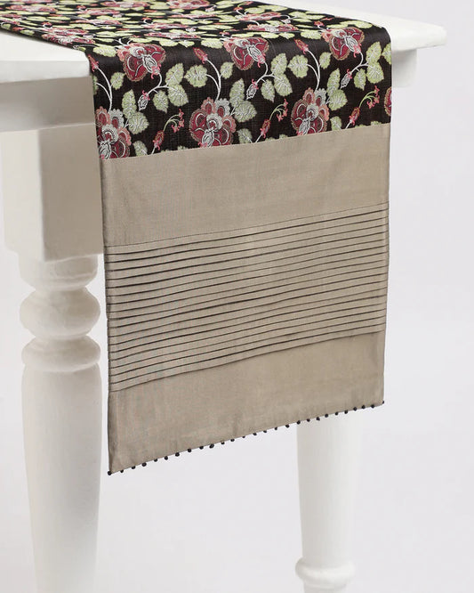 Forest Floor Tanchoi silk table runner with botanical patterns and hand-tucked taupe pleats draped over a white table.