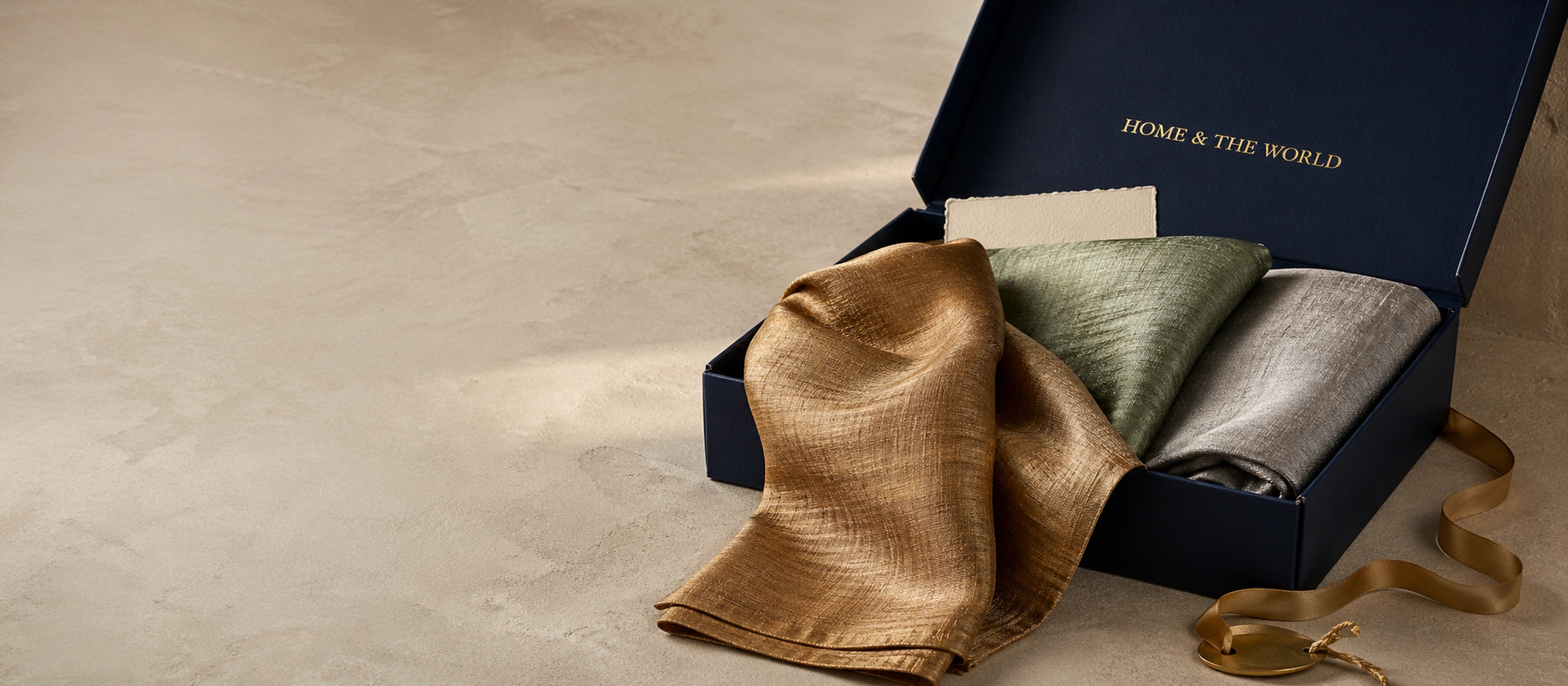 Home & the World luxury housewarming gift box with bronze, sage, and silver silk cushion covers.