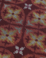 Macro view of the Hearth runner center: gold and silver-grey floral-geometric ikat motifs on a deep burgundy silk field.
