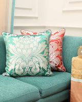 A 20x20 Mint and Silver Lotus Gyasar pillow styled on a teal sofa next to a cream  and pink silk cushion.
